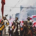 rekonstruktorzy na koniach w paradzie wśród powiewających polskich flag