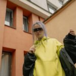 Kobieta w neonowej bluzie z kapturem i okularach na tle miasta