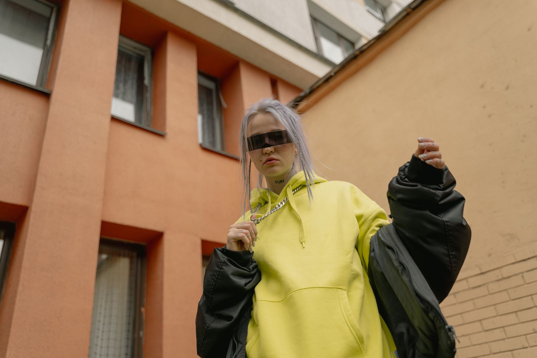 Kobieta w neonowej bluzie z kapturem i okularach na tle miasta